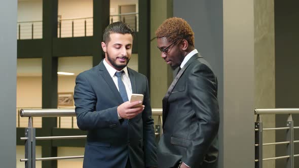 Two multiethnic managers standing in the corridor with mobile phone