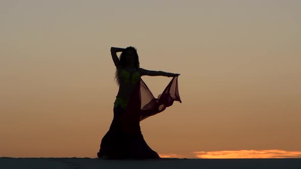 Girl Gracefully Dances with a Veil of Hands Against a Sunset. Silhouette