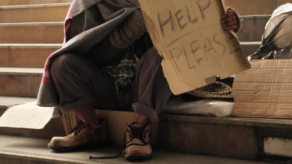 Homeless old man in dirty clothes sitting on the street and asking for help