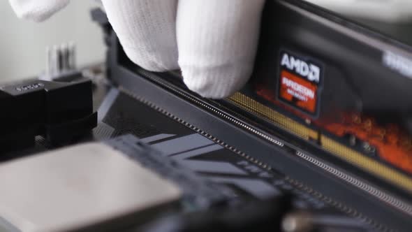 A tech specialist's hand in white gloves installs the RAM in the motherboard