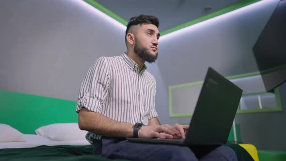 Concentrated Young Male Freelancer Typing on Laptop Keyboard in Slow Motion Thinking Sitting in