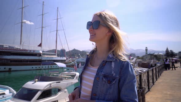 young beautiful woman smiles against background of pier, next to modern boats