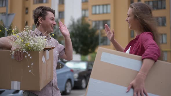 Happy Husband and Wife Gesturing Highfive in Slow Motion Standing with Parcels at Building Moving in