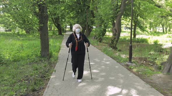 Active Senior Old Woman in Mask Training Nordic Walking in Park at Quarantine