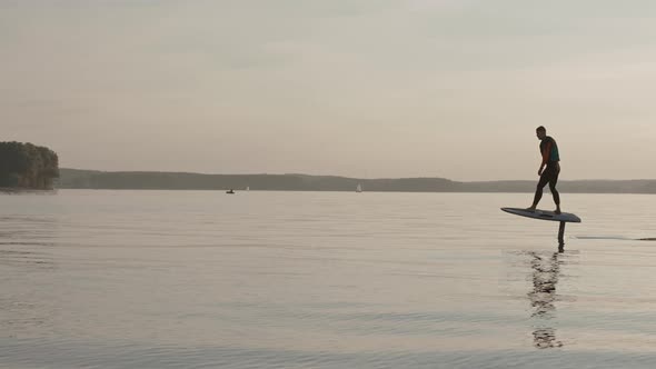 Man Riding on a Hydrofoil Surfboard on Large Lake at Warm Sunset