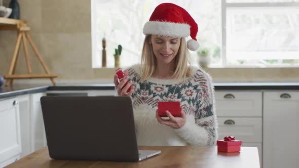 Woman opening gift box while having a video call on laptop