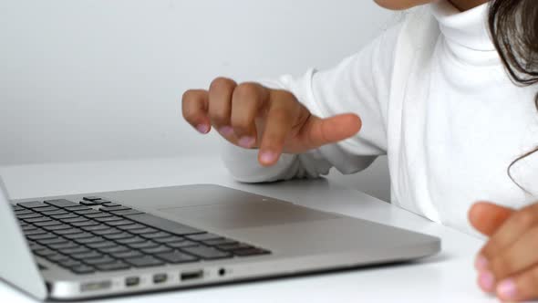 A child girl on distance learning sits in front of a laptop and does homework.