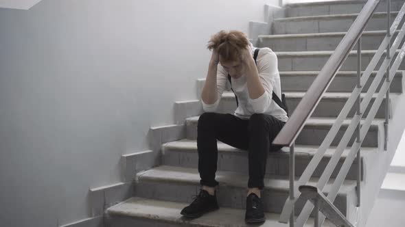 Wide Shot of Stressed Bullied Redhead Teenager Sitting on High School Stairs and Thinking