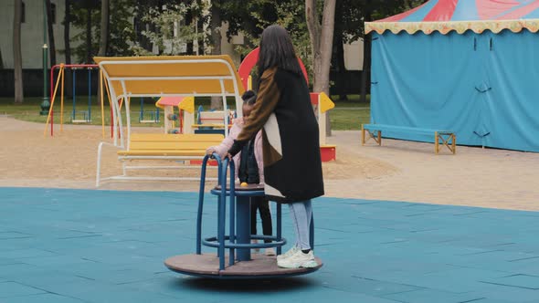 Young Friendly Family Walking on Playground Little Girl Spins Mother on Carousel Child Fast Rides