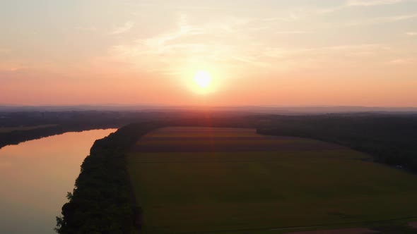 Farmland surrounds the Potomac river as a drone flies over during orange sunset aerial