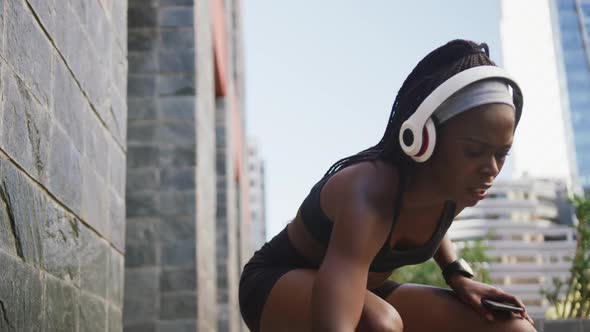 African american woman exercising outdoors wearing wireless headphone taking rest in the city