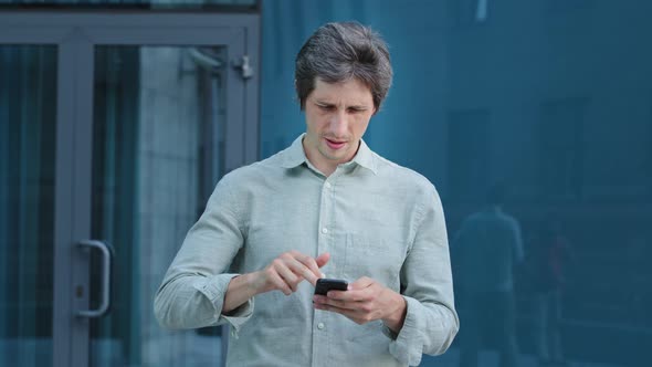 Angry Annoyed Young Businessman Holding Using Texting on Smartphone Frustrated By Stuck Broken Phone