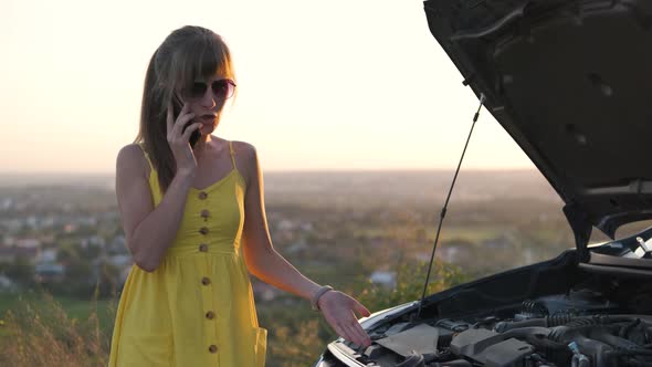 Stranded Female Driver Talking on Cell Phone Standing Near Her Vehicle with Open Hood Having Engine