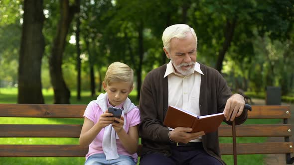 Boy Using Smartphone While Granddad Reading Book, Concept of Technology vs Paper