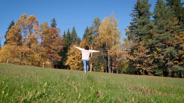 Woman Joyfully Running Across Green Lawn With Her Hands Raised To Side