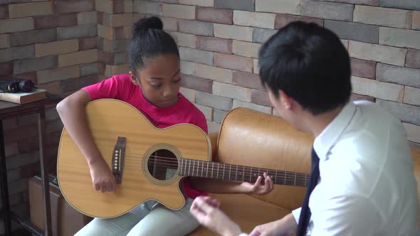 Young Asian Male Teacher Giving a Guitar Lesson and Teaching How to Play Guitar to Little Girl