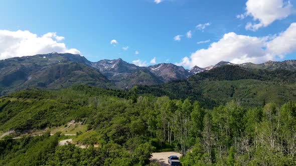 Pull back aerial view of a mountain road with a truck parked along the trail and rugged mountains in