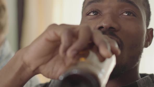 Portrait of Confident African American Man Talking and Drinking Beer with Friends at Home. Leisure