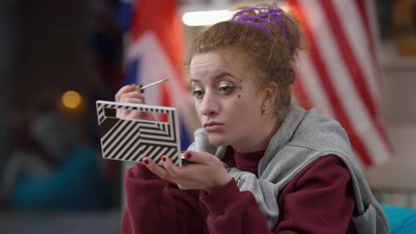 Concentrated Hipster Young Woman Applying Shiny Makeup at Home in the Evening