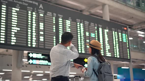 Couple traveler checking flight schedule board in airport terminal