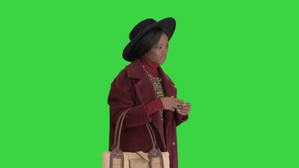 African American Fashion Girl in Coat and Black Hat Posing with a Handbag on a Green Screen Chroma