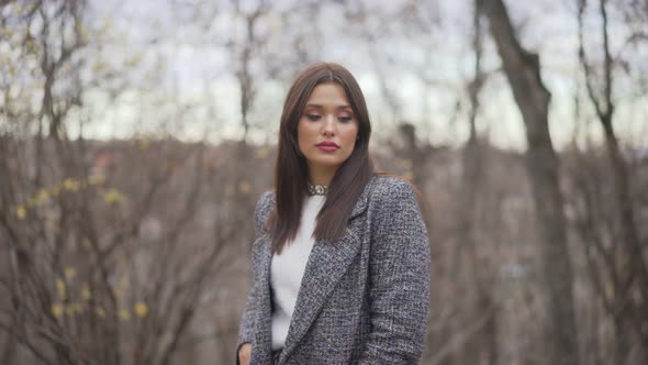 Young Beautiful Stylish Girl with Long Dark Hair Walking Outdoors in Gray Coat at Sunset. Closeup