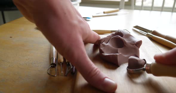 An artist carving and cutting brown modeling clay with a metal tool before sculpting and shaping the