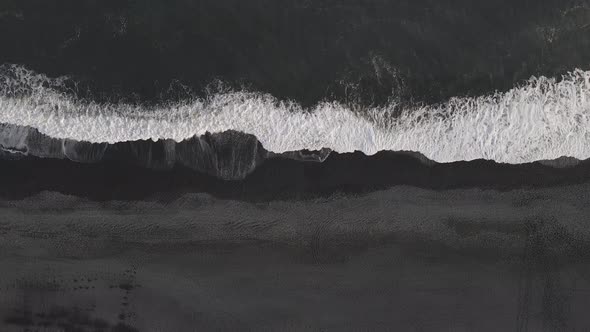 Waves breaking on black sand beach in Iceland. Aerial top down descendent