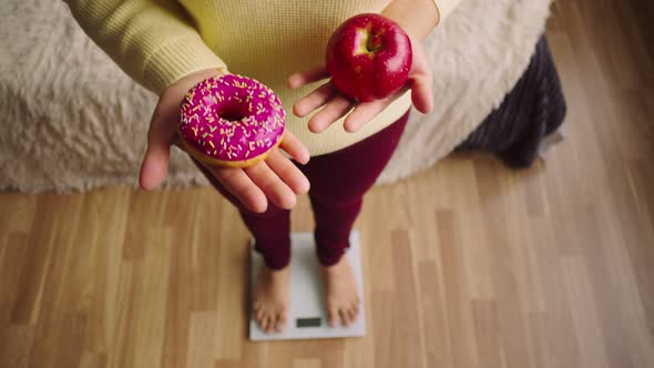 Woman Stands on Scale and Holds Donut and Apple in His Hands