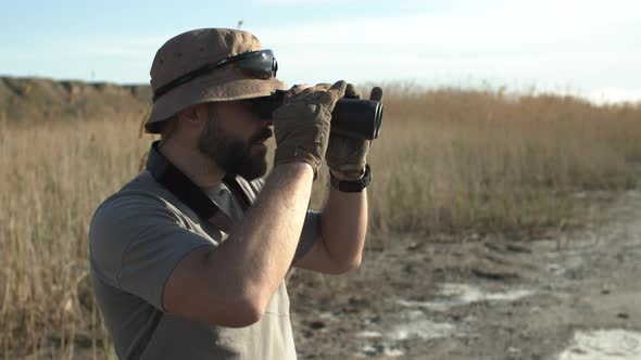 Outdoor Side Shot of Bearded Man Soldier in Hat and Military Tshirt Looking Through Binoculars