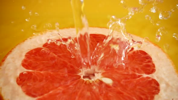Half of a grapefruit in a jet of water on an orange background. Slow motion.