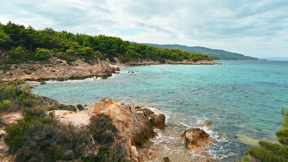 Aegean sea rocky coast with greenery around at cloudy weather. Bushes and trees, blue water. Greece