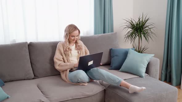 Blonde Girl Sitting on the Couch Working on a Laptop