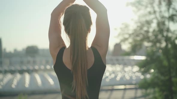 Back View of Slim Caucasian Brunette Woman with Ponytail Standing in Sunrays with Raised Hands