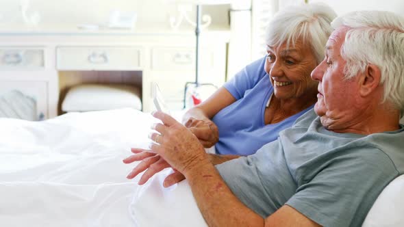 Smiling couple lying on bed and using digital tablet in bedroom