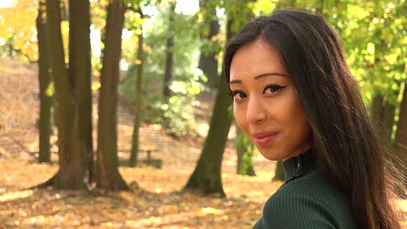 A Young Asian Woman Turns and Smiles at The Camera in A Park