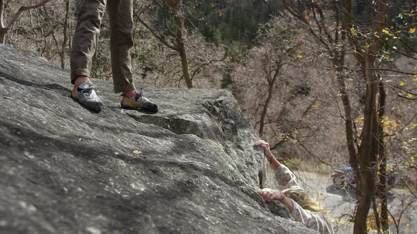 Woman climbing up boulder has she reaches for help to make it to the top