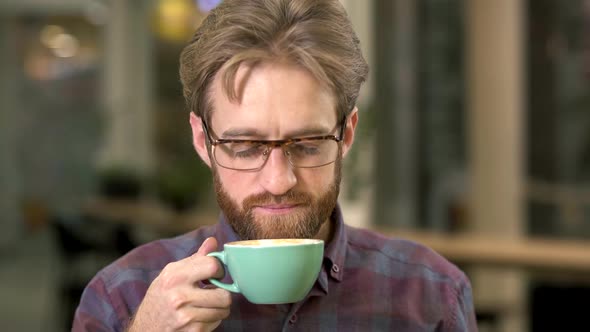 Portrait of Joyful Bearded Man in Glasses Drinking Coffee Close Up. Beardie Clos Eyes Enjoys His