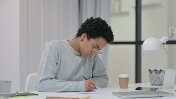 Young African Woman Writing on Paper at Work