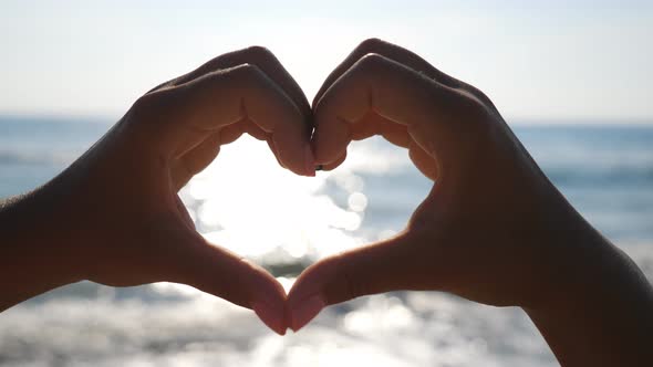 Woman Making Heart Through Her Hands with Seascape at Background. Close Up of Female Arms Showing