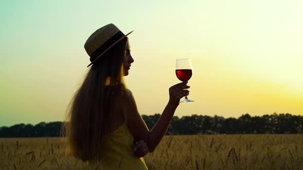 Silhouette of girl with glass of wine in wheat field