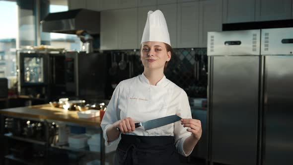 Professional kitchen, portrait: Female Chef holding a knife and looking at the camera