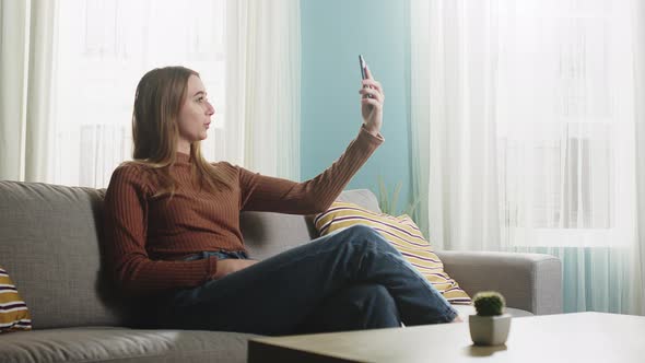 Young Girl Is Sitting on a Sofa and Talking on a Video Call