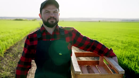 Man Farmer Walks Through Field with Basket of Crops and Shovel