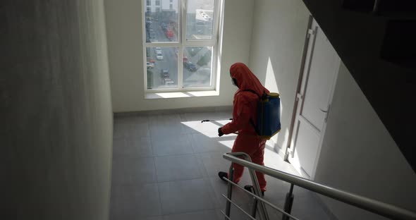 A Man In Protective Gear Disinfects A Sprayer In The Entrance Of A Multi-storey Building. 