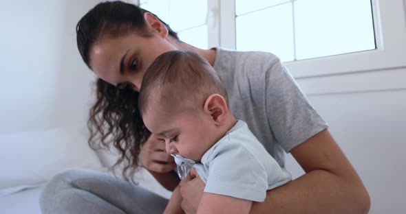 Young loving mother holding her baby on bed at home