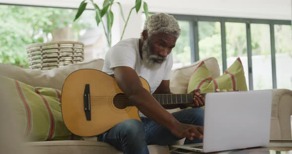Video of sad african american senior man playing the guitar and using laptop