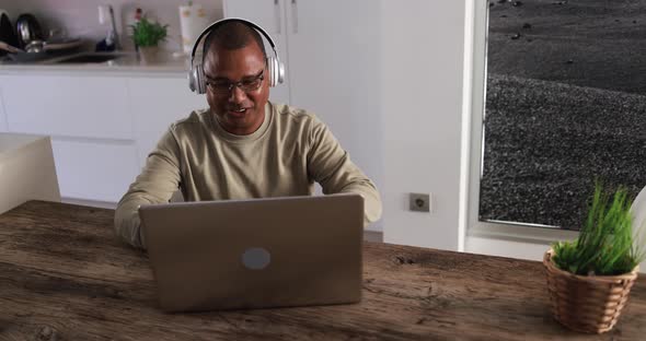 Senior african man doing video call with computer laptop while wearing headphones at home