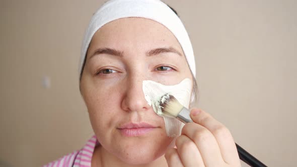 Young Woman Applying Cosmetic Mask with a Brush to Face