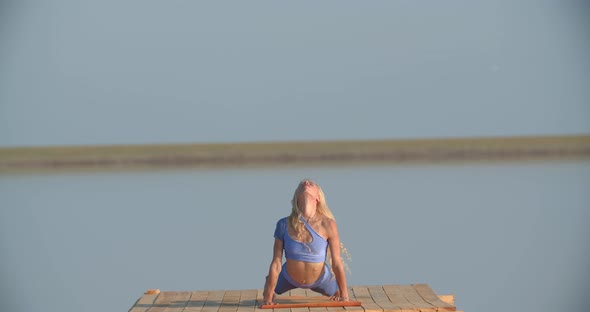 Athletic Young Woman is Stretching and Doing Yoga on a Platform at the Lake